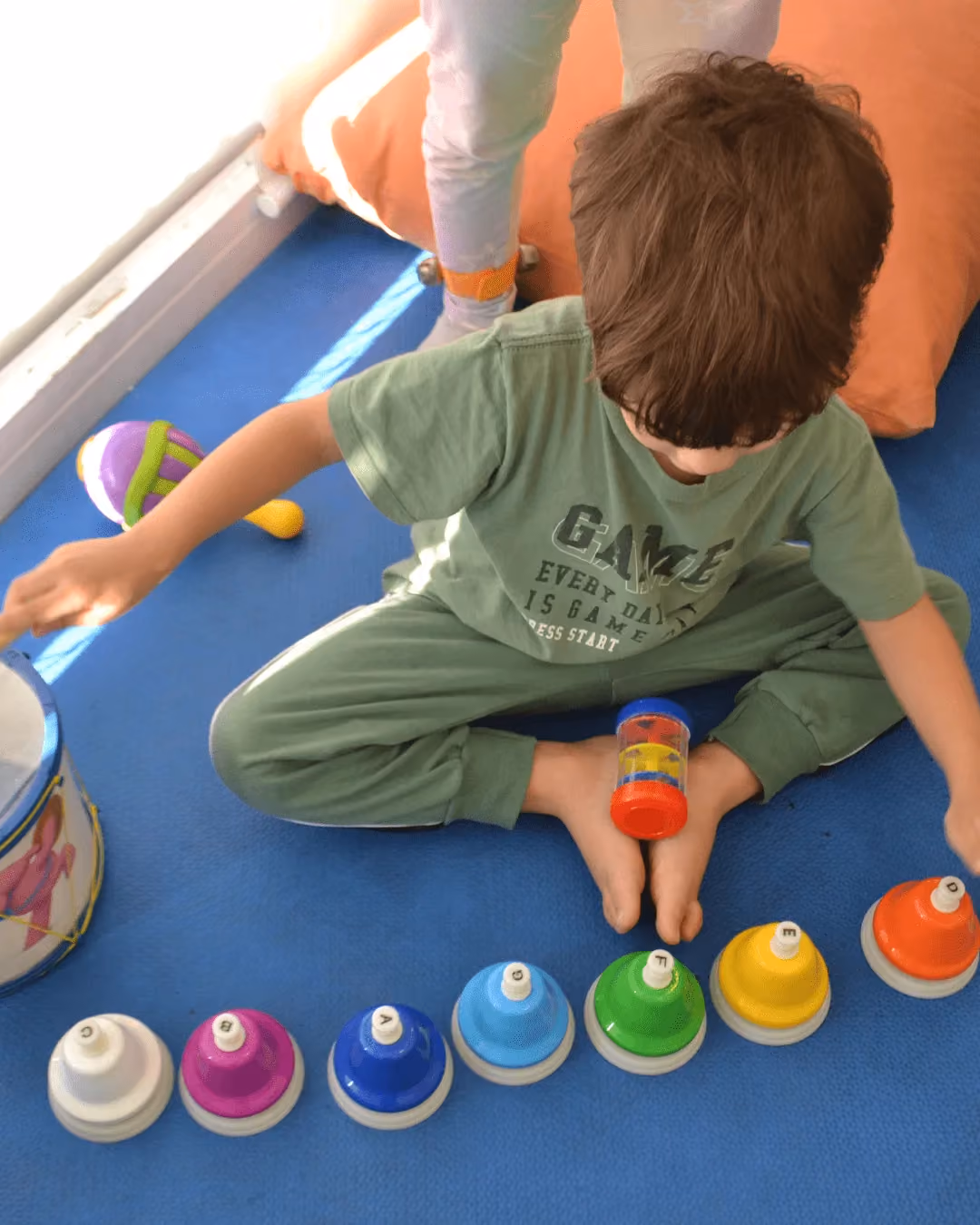 Criança tocando sinos coloridos sentada no tatame.