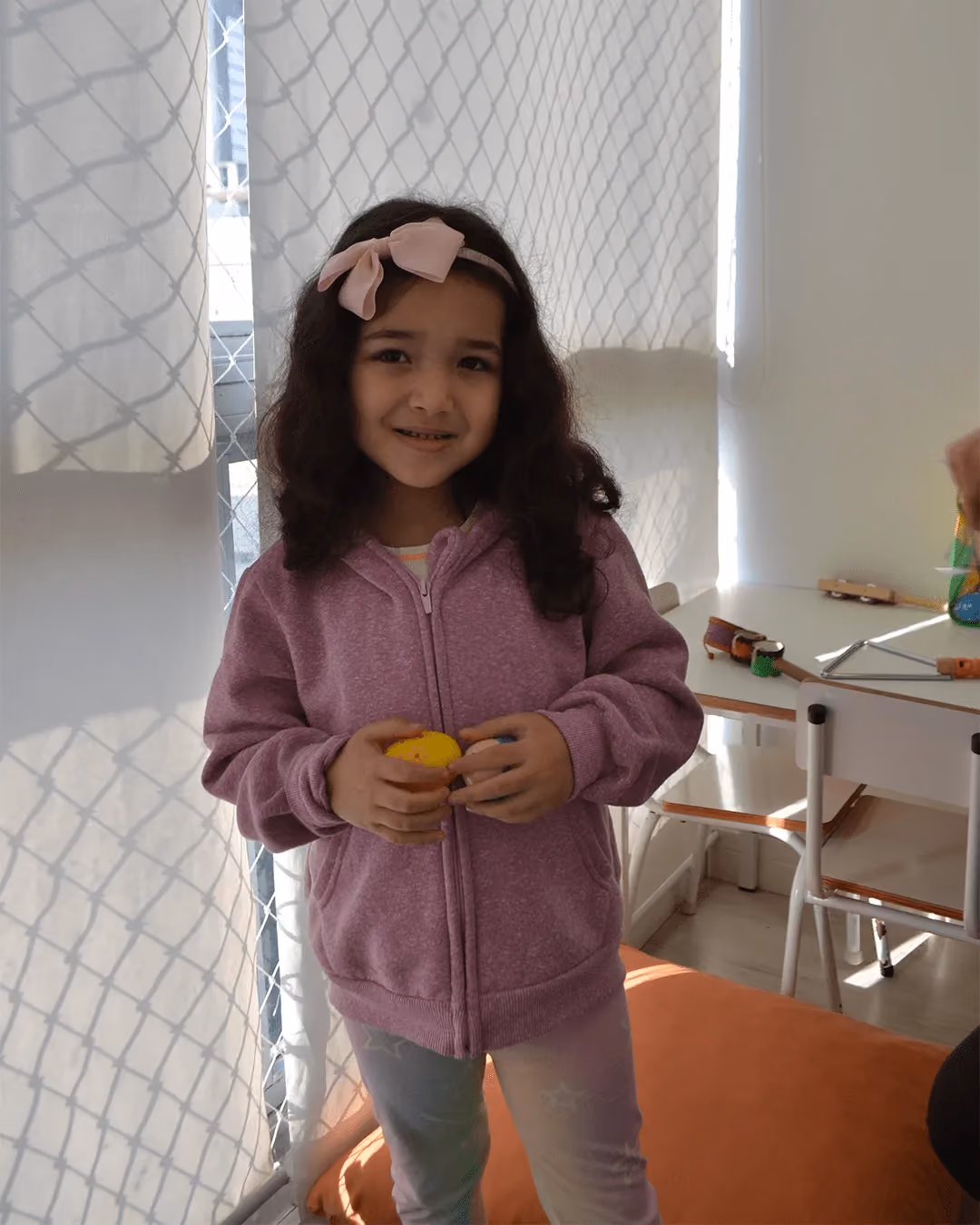 Criança com tiara segurando um chocalho durante a atividade de música.