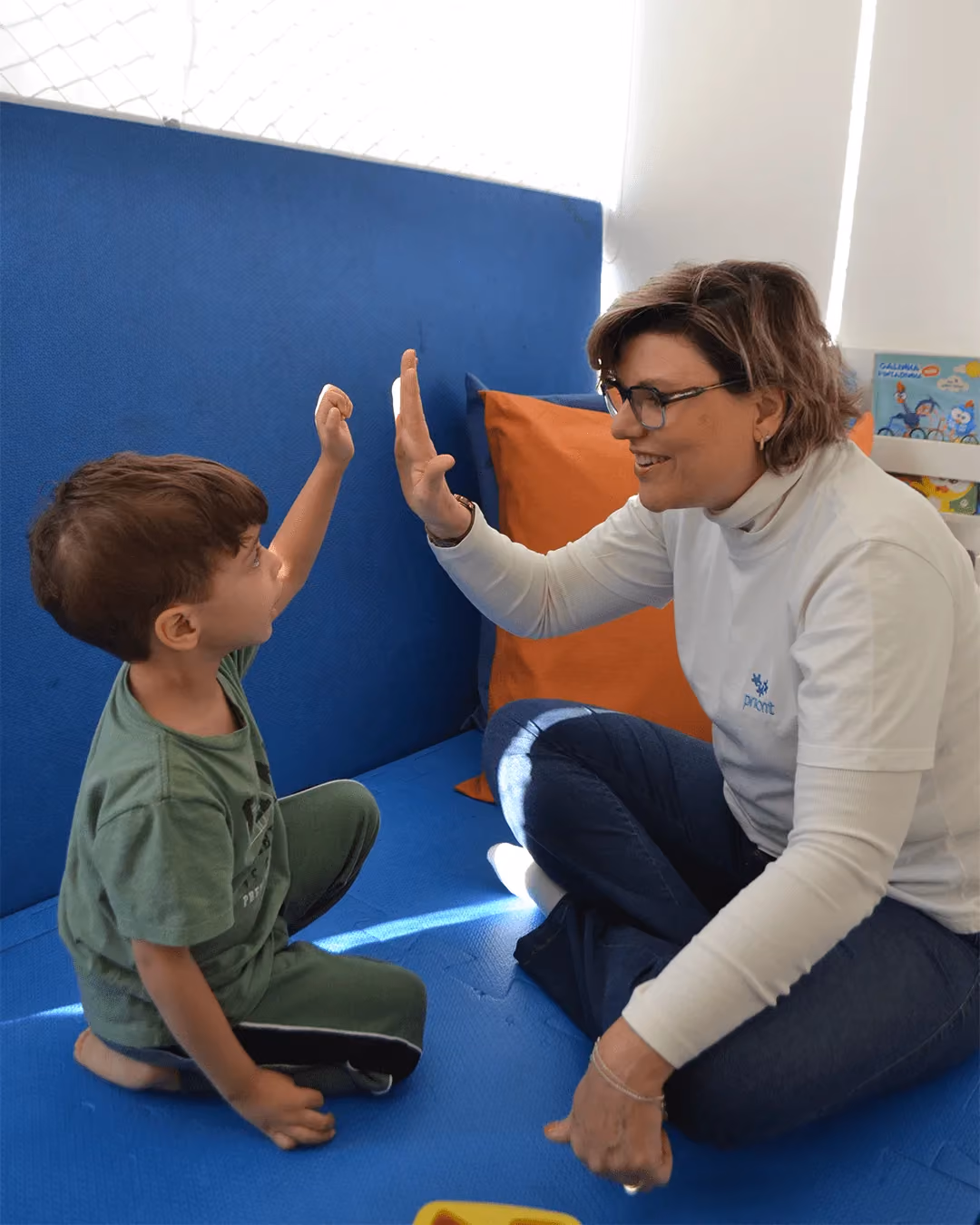 Criança e fonoaudióloga comemorando de mãos erguidas durante a sessão. - 2 de 5
