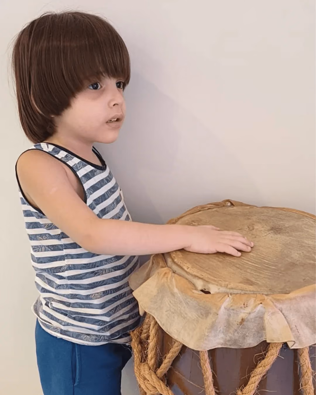 Child in a striped shirt playing an atabaque drum during the capoeira class. - 2 de 4