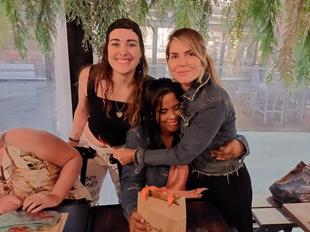 Três participantes do grupo abraçadas durante um passeio ao ar livre.
