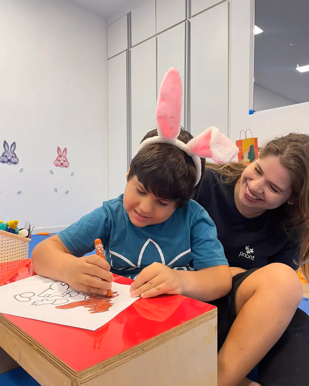 Criança desenhando em prancha inclinada ao lado da terapeuta.