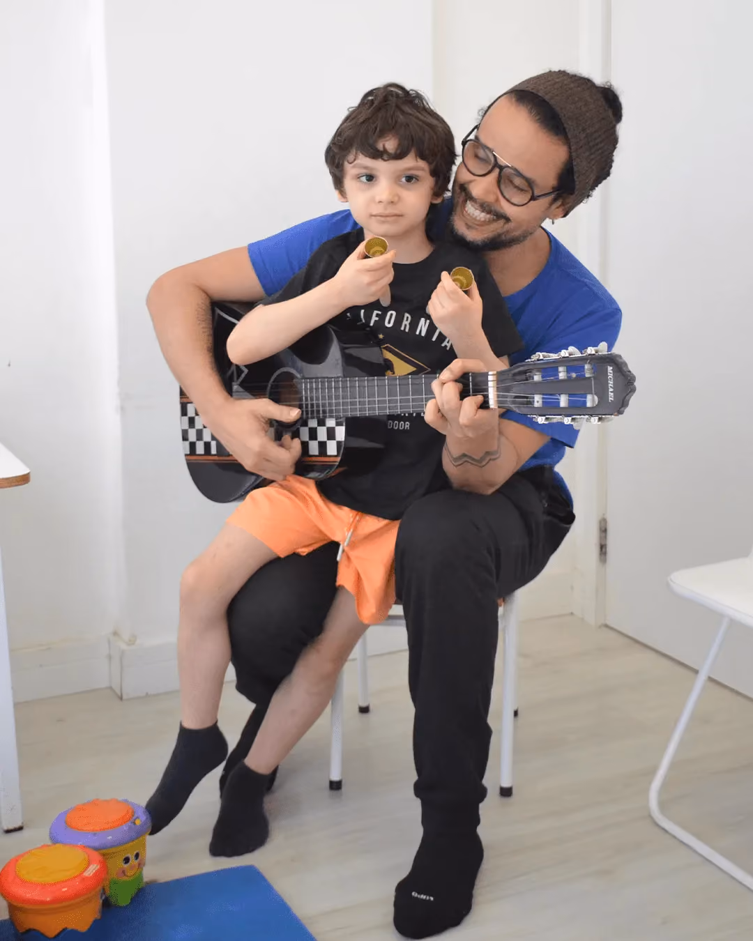 Terapeuta com violão e criança sentados juntos na atividade de música. - 3 de 4
