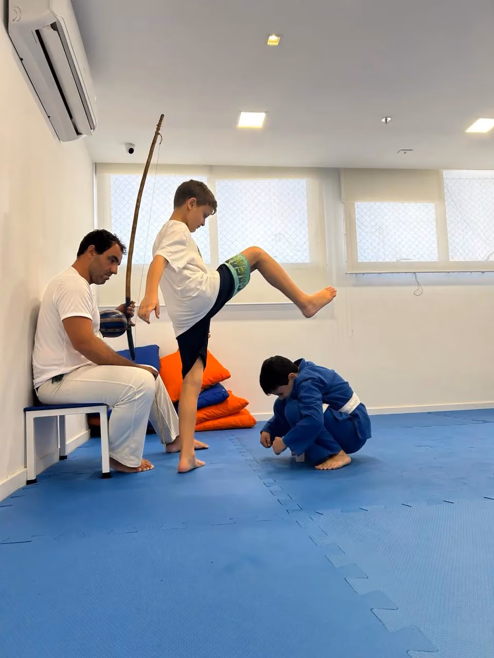 Instructor and child performing a capoeira movement on the blue mat.