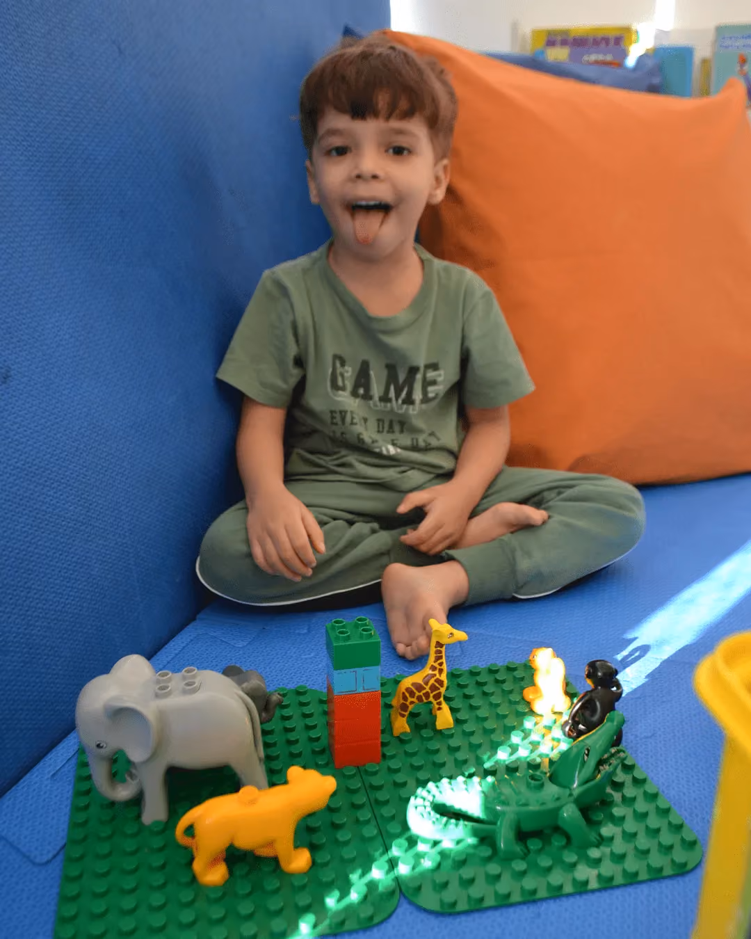 Criança sorrindo ao lado de uma base de blocos montada com animais de brinquedo. - 4 de 5