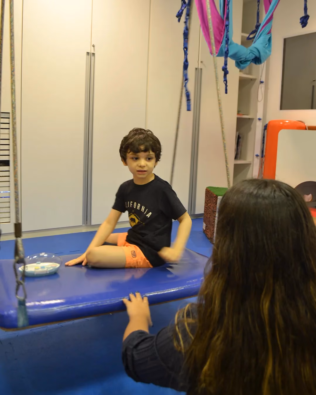 Criança sobre a plataforma acolchoada em atendimento de terapia ocupacional.