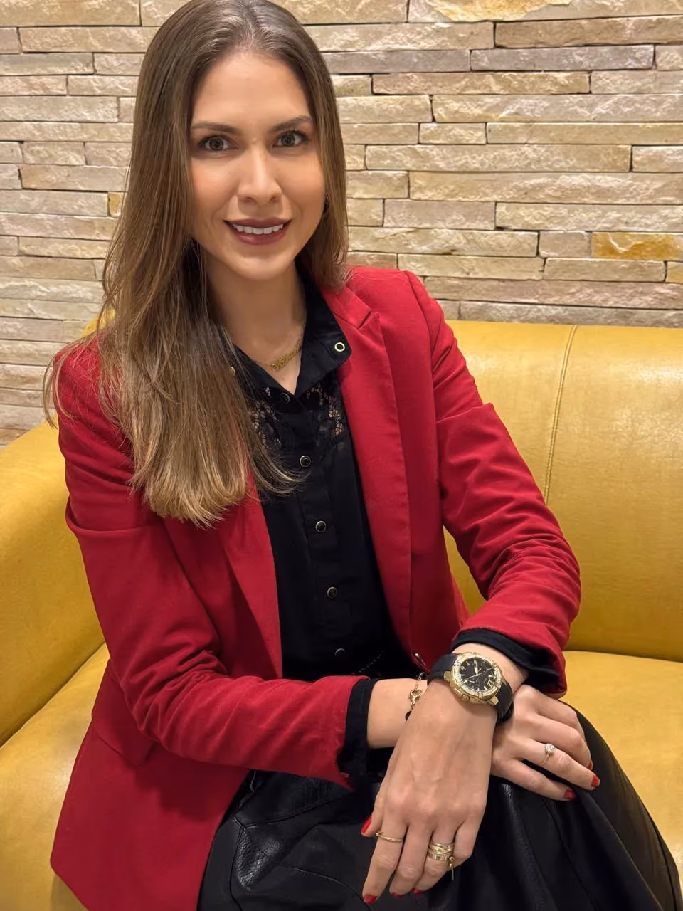 Dr. Tathiana de Almeida Martins de Souza sitting on a yellow sofa, wearing a red blazer